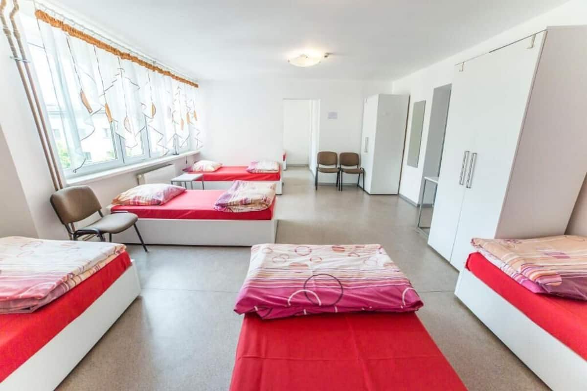Un dormitorio con tres camas, una ventana con cortinas, una silla y un armario.