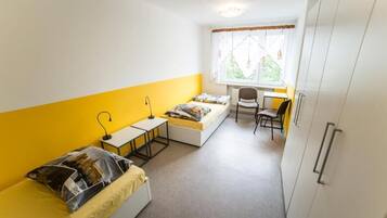A compact room with a bed, a desk, a chair, and a window with curtains.