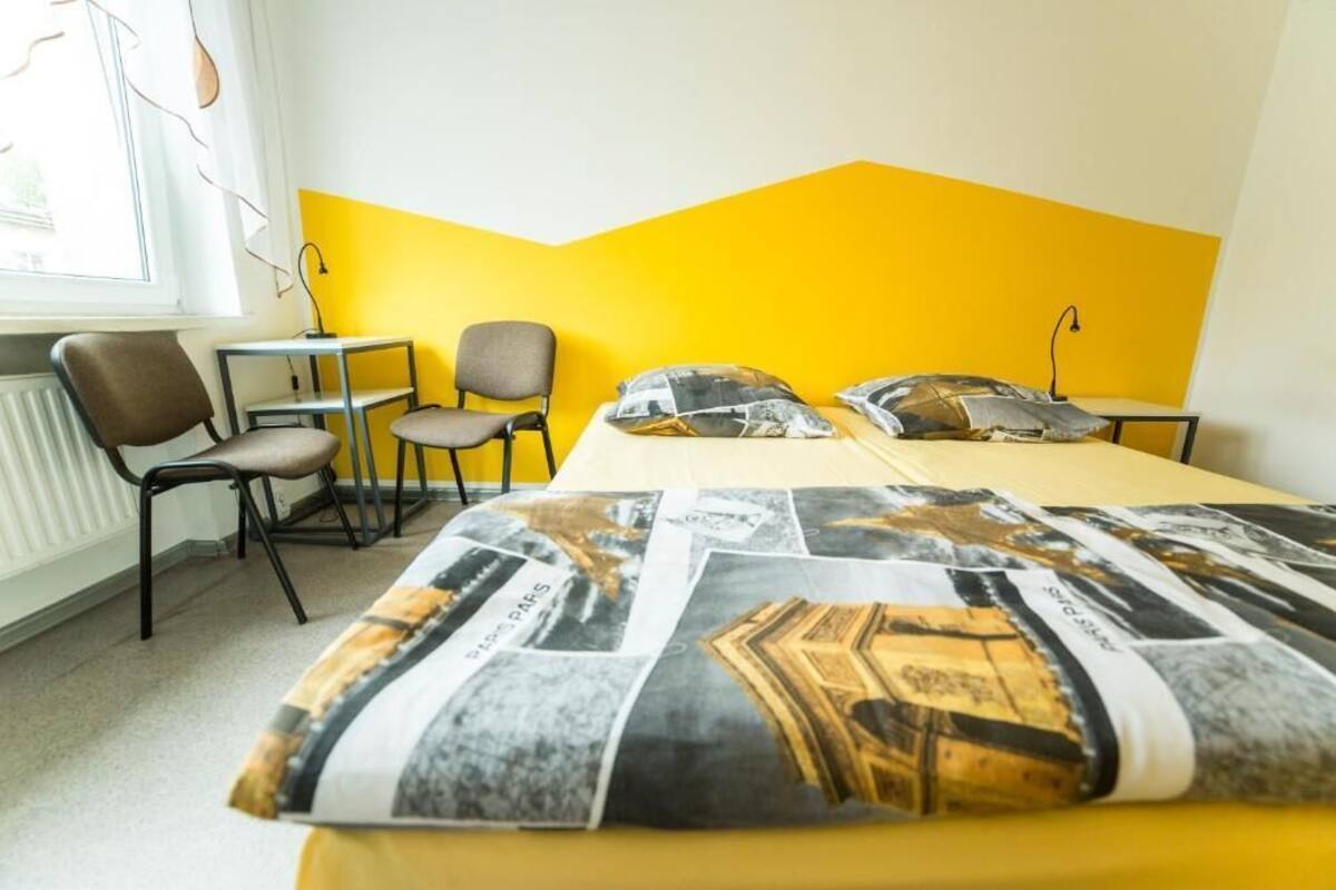 Una habitación de hotel con una cama, dos sillas, una mesita y una ventana.