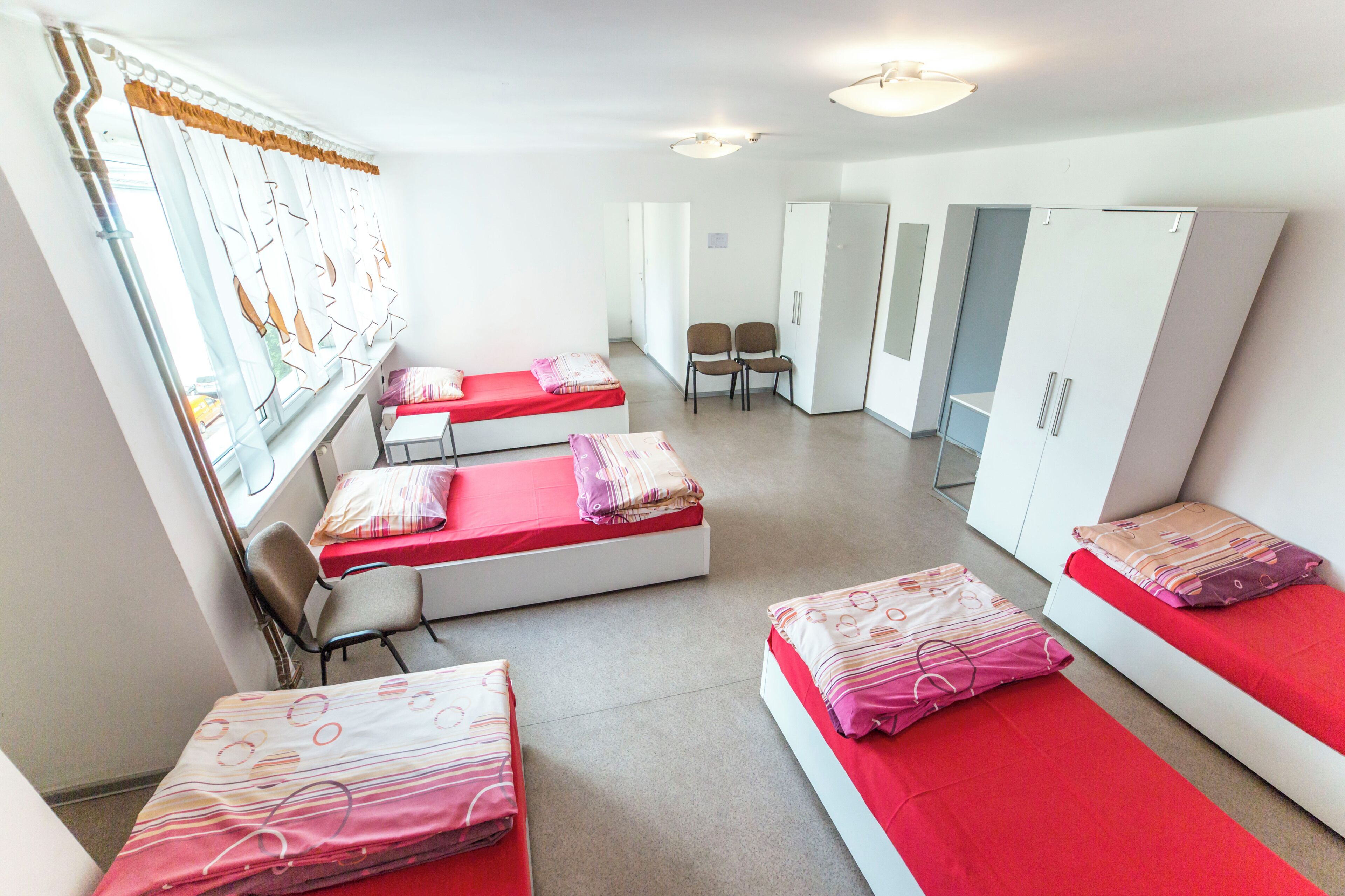 Habitación tipo dormitorio con tres camas individuales, un armario, un escritorio y una ventana con cortinas.