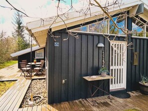 Uma cabana pequena e escura com varanda, uma porta com o número 52 e uma mesa com cadeiras do lado de fora.