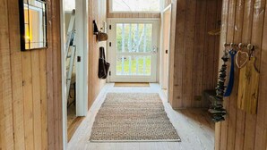 Un passadís interior de fusta amb una porta que dóna a l'exterior, una petita catifa i un penjador amb objectes.