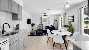 A modern kitchen with white cabinets, a black faucet, and a dining area with white chairs and a round table. - Fisherman's Cottage - 2 bd/1 bath apartment in Naples park! Close to beaches! (Naples)