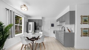 A modern kitchen with grey cabinets, a stainless steel refrigerator, and a dining area with a round table and white chairs. - Fisherman's Cottage - 2 bd/1 bath apartment in Naples park! Close to beaches! (Naples)