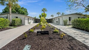 A row of single-story buildings with a central pathway, surrounded by greenery and palm trees. - Fisherman's Cottage - 2 bd/1 bath apartment in Naples park! Close to beaches! (Naples)