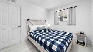 A bedroom with a bed, a nightstand, a window with curtains, and a door. - Fisherman's Cottage - 2 bd/1 bath apartment in Naples park! Close to beaches! (Naples)