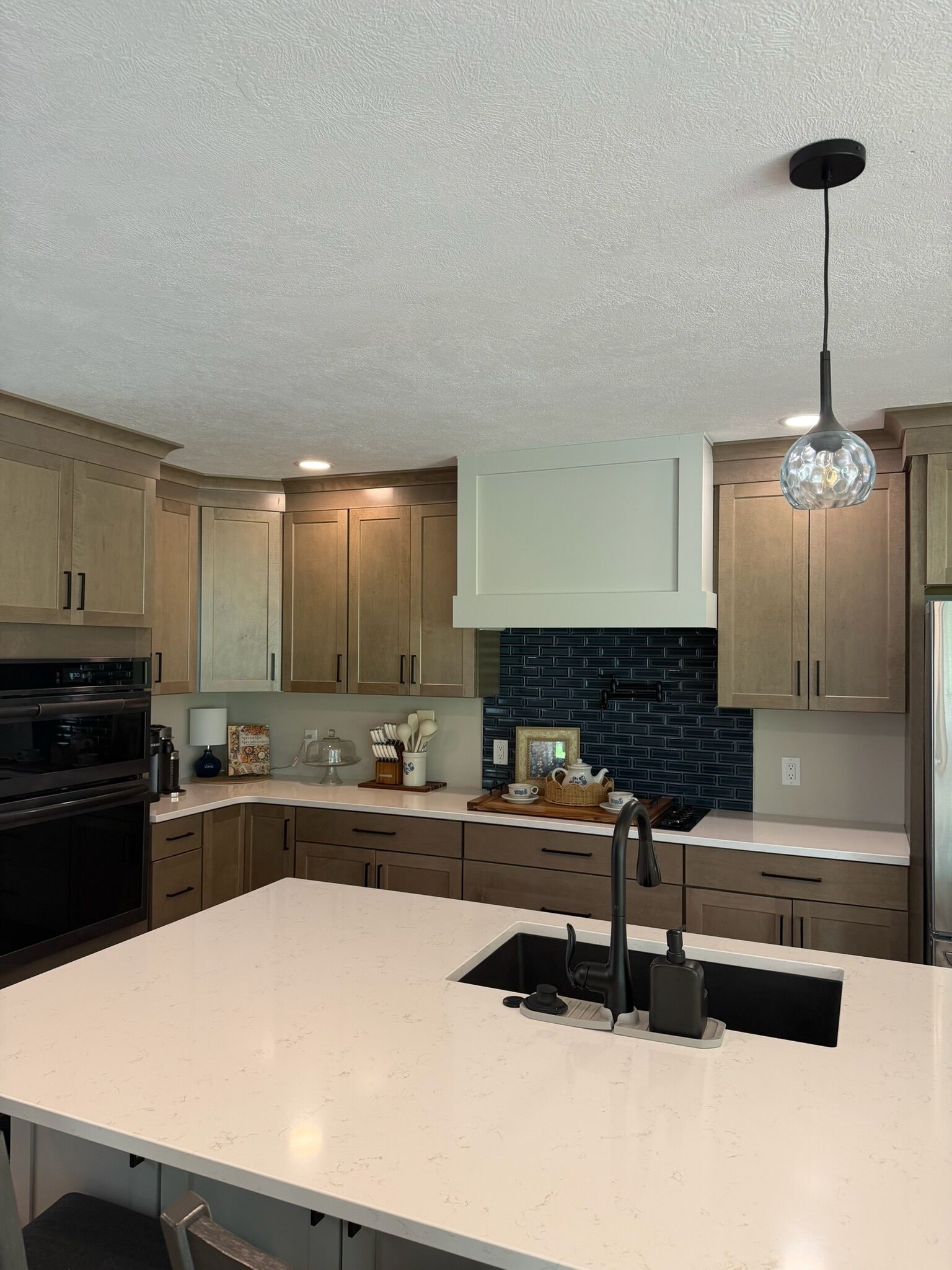 A modern kitchen with a large island, stainless steel appliances, and a black pendant light.