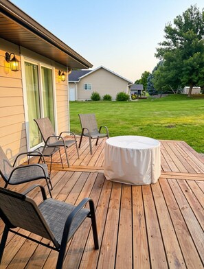 Una terraza con mobiliario exterior, incluyendo sillas y una mesa redonda, y una casa al fondo.