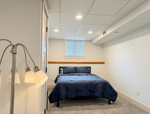 Een slaapkamer met een bed, een nachtkastje, een lamp, een raam en een plafond met inbouwverlichting.