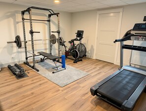 Un gimnasio en casa con una banca de pesas, una estructura para sentadillas, mancuernas, una elíptica y una cinta de correr.