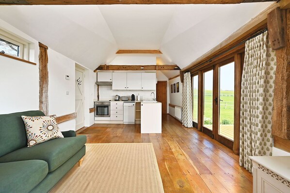 A spacious living room with a green sofa and a kitchen area with white cabinets and a central island. - Acorn Barn - a holiday let that sleeps 2 guests in 1 bedroom (Ashford)