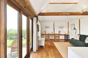 A room with a dining table, chairs, a sofa, and a view of a green landscape through large windows.