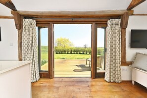 A room with a wooden floor, a bench, and a view of a vineyard through large glass doors. - Acorn Barn - a holiday let that sleeps 2 guests in 1 bedroom (Ashford)