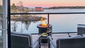 A balcony with wicker furniture, a fire pit, and a table with a bottle and glasses. - A Little piece of Paradise - stunning ocean views! (Lunenburg)