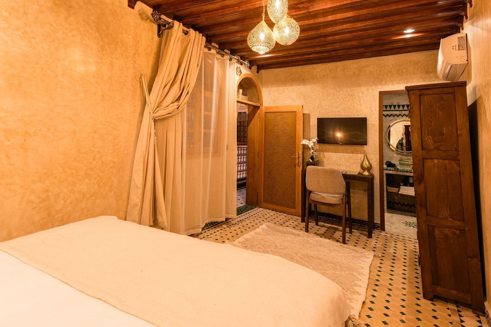 A bedroom with a bed, a chair, a desk, a wardrobe, and a mirror.