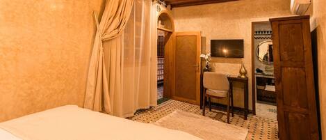 A bedroom with a bed, a chair, a desk, a wardrobe, and a mirror.