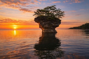 A natural rock formation with trees on top, surrounded by calm water and a sunset. - Garfield Inn Hotel - 2 Bedroom suite (Port Austin)