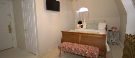 A bedroom with a bed, bench, TV, and a chandelier.
