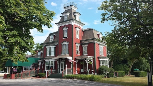 A red Victorian-style building with a prominent tower, a front porch with a railing, and a green awning. - Garfield Inn Hotel - 2 Bedroom suite (Port Austin)
