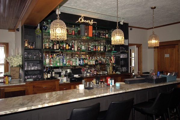 Zona de bar con un letrero de neón, estantes llenos de botellas e lámparas colgantes.