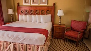 Ein Hotelzimmer mit einem großen Bett, einem Holzkopfteil, einem Nachttisch, einem roten Sessel und einem karierten Boden.