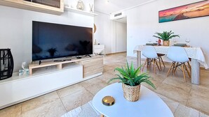 A modern living room with a large flat-screen TV, a dining area with a table and chairs, and a painting on the wall. - Stylish Apartment in Central Location (San Pedro del Pinatar)