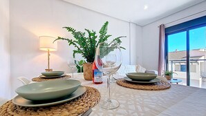 A dining table set with plates, a wine glass, and a bottle, surrounded by woven placemats and a potted plant. - Stylish Apartment in Central Location (San Pedro del Pinatar)