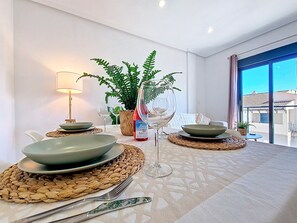 A dining table set with plates, a wine glass, and a bottle, surrounded by woven placemats and a potted plant. - Stylish Apartment in Central Location (San Pedro del Pinatar)