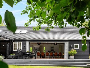 A modern house with a dark exterior, a tiled roof, and a covered outdoor seating area with chairs and a table. - 4 Star Holiday Home in Vig (Vig)