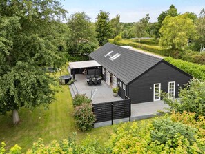 A black building with a sloped roof, a covered patio with outdoor furniture, and a hot tub. - 4 Star Holiday Home in Vig (Vig)