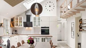 A modern kitchen with white cabinetry, a dining area with a long table, and a clock on the wall. - 4 Star Holiday Home in Vig (Vig)