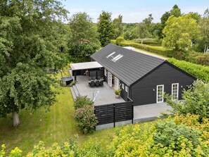 A black building with a sloped roof, a covered patio with outdoor furniture, and a garden area. - 4 Star Holiday Home in Vig (Vig)