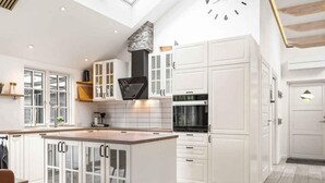 A modern kitchen with white cabinetry, a central island with glass doors, a built-in oven, and a clock on the wall. - 4 Star Holiday Home in Vig (Vig)
