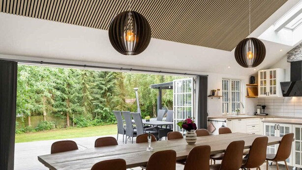 A modern kitchen with white cabinets, a black range hood, and a dining area with a wooden table and brown chairs. - 4 Star Holiday Home in Vig (Vig)
