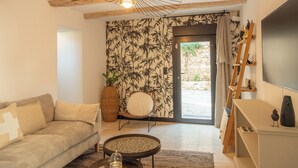 Un salon comprenant un canapé, une table basse, un téléviseur fixé au mur, une lampe décorative et une porte donnant sur un espace extérieur.