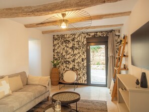 Ein Wohnzimmer mit Sofa, Couchtisch, Wand-Fernseher, dekorativer Lampe und einer Tür zu einem Außenbereich.