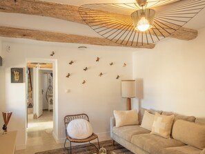 Ein gemütliches Wohnzimmer mit Holzbalkendecke, einem Korbsessel, einer Couch mit Kissen, einer Lampe und Wandstickern mit Schmetterlingsmotiven.