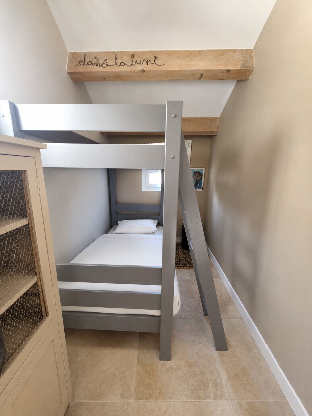 Ein Stockbett mit Holz-Kopfteil, einem kleinen Fenster und einer Treppe.