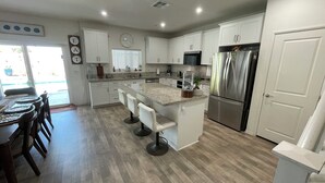 A modern kitchen with white cabinets, a stainless steel refrigerator, a granite countertop, and a dining area with wooden chairs. - Fabulous 6-bedroom townhome with AC in sunny Indio (Indio)