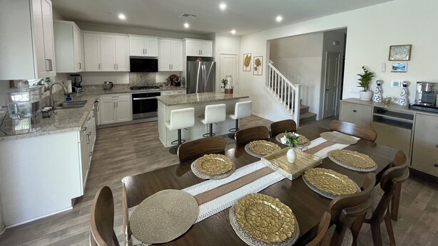 A modern kitchen with white cabinets, a central island, and a dining area with a wooden table and chairs. - Fabulous 6-bedroom townhome with AC in sunny Indio (Indio)