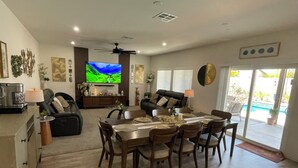 A spacious living room with a dining area, a flat-screen TV, ceiling fan, and a view of the outdoors. - Fabulous 6-bedroom townhome with AC in sunny Indio (Indio)
