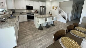 A modern kitchen with white cabinets, stainless steel appliances, and a central island with bar stools. - Fabulous 6-bedroom townhome with AC in sunny Indio (Indio)