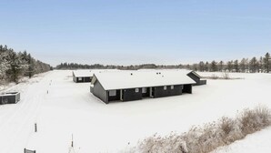 Schneebedecktes Gelände mit mehreren Gebäuden, darunter ein großes, schwarzes Gebäude mit vielen Fenstern und ein kleineres, angrenzendes Bauwerk.
