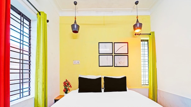 A hotel room with a bed, two wall-mounted lights, a window with bars, and a door with curtains. - Hotel O Thammanam Kochi (Kanayannur)