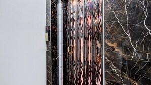 Metallinen portti, jossa on geometrinen kuvio, marmoriseinä valkoisilla juonteilla ja valkoinen ovikehys.