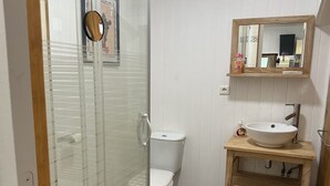 A bathroom with a glass shower enclosure, a white toilet, a wooden vanity with a sink, and wicker baskets. - I'm renting a 2-person wooden chalet from April 01 to May 20, 2026. (Salernes)