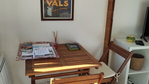 A wooden table with a chair, a framed poster on the wall, and a shelf with a basket and a remote control. - I'm renting a 2-person wooden chalet from April 01 to May 20, 2026. (Salernes)