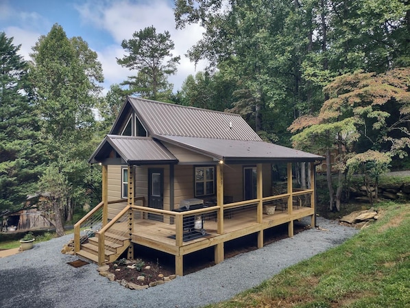 A cabin with a wooden deck, a staircase, and a metal roof, surrounded by trees. - Cozy Creekside Cabin in Bryson City, North Carolina (Bryson City)