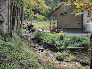 A cabin with a covered porch, a small stream, and surrounding greenery. - Cozy Creekside Cabin in Bryson City, North Carolina (Bryson City)