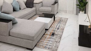 Ein modernes Wohnzimmer mit einem Ecksofa, einem Couchtisch, einem gemusterten Teppich und einem Fernseher auf einem Schrank.